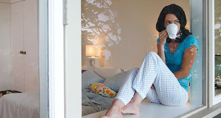 woman in pajamas drinking coffee from window
